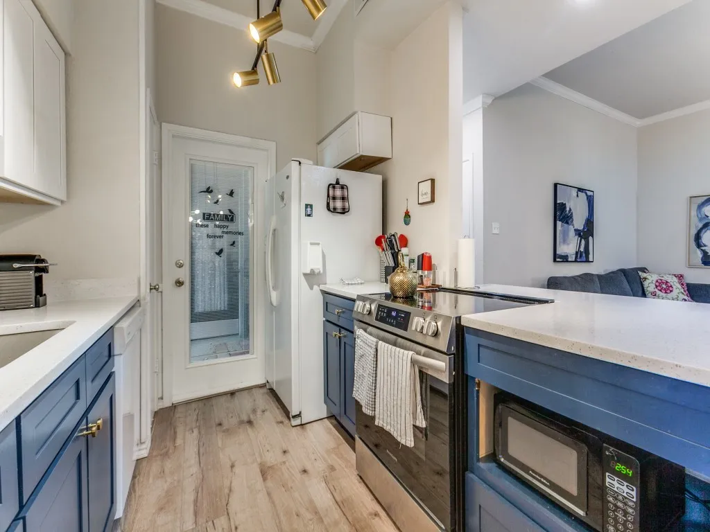 Kitchen with white appliances, blue cabinets, light stone countertops, and ornamental molding