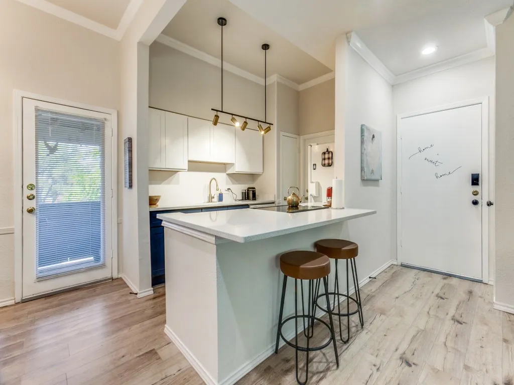 Kitchen featuring white cabinets, a breakfast bar, a peninsula, decorative light fixtures, and light wood-style flooring