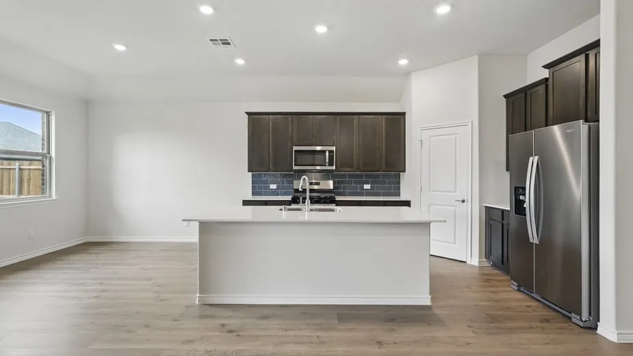 Open-concept kitchen featuring an island with a sink, stainless steel appliances, dark wood-finish cabinetry, and a subway tile backsplash
