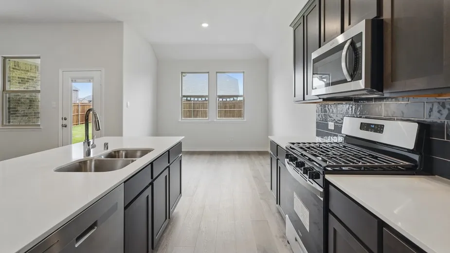 Kitchen featuring a spacious island with dual stainless steel sinks, white countertops, dark cabinetry, stainless steel appliances, and a dark subway tile backsplash