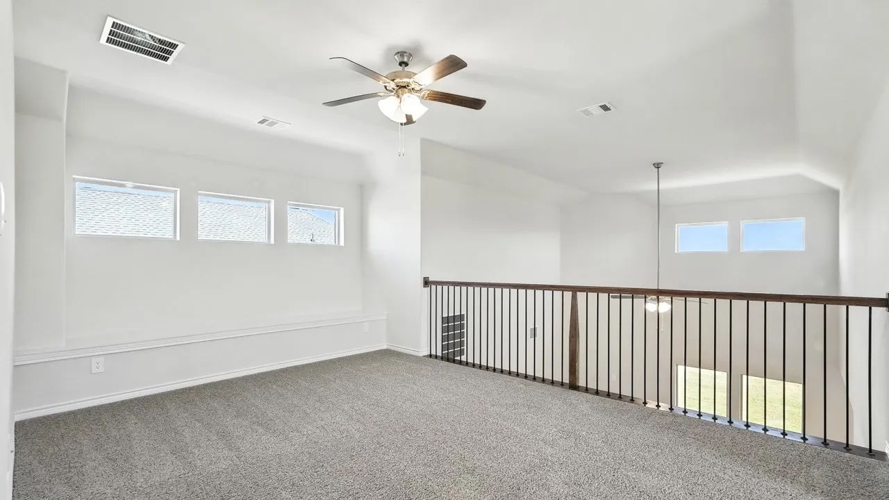 Carpeted loft featuring a ceiling fan with light, multiple windows, and a wood-finish railing with metal spindles