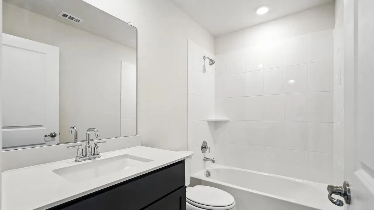 Bathroom featuring a dark wood-finish vanity with a light countertop, chrome faucet, wall-mounted mirror, and a white tiled shower/tub combination with chrome fixtures and a recessed light