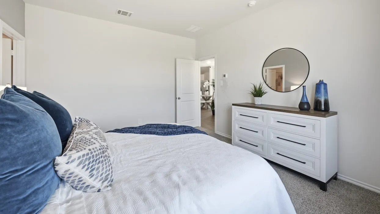 Bedroom featuring light gray walls, plush gray carpet, a white six-drawer dresser with a dark wood-finish top, and a circular wall-mounted mirror