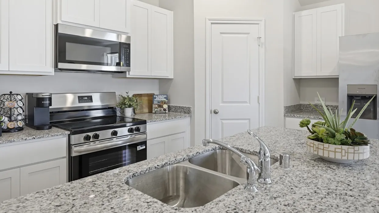 Kitchen featuring a large central island with a double basin sink and chrome faucet, light-toned stone countertops, white cabinetry, and stainless steel appliances including a range and microwave