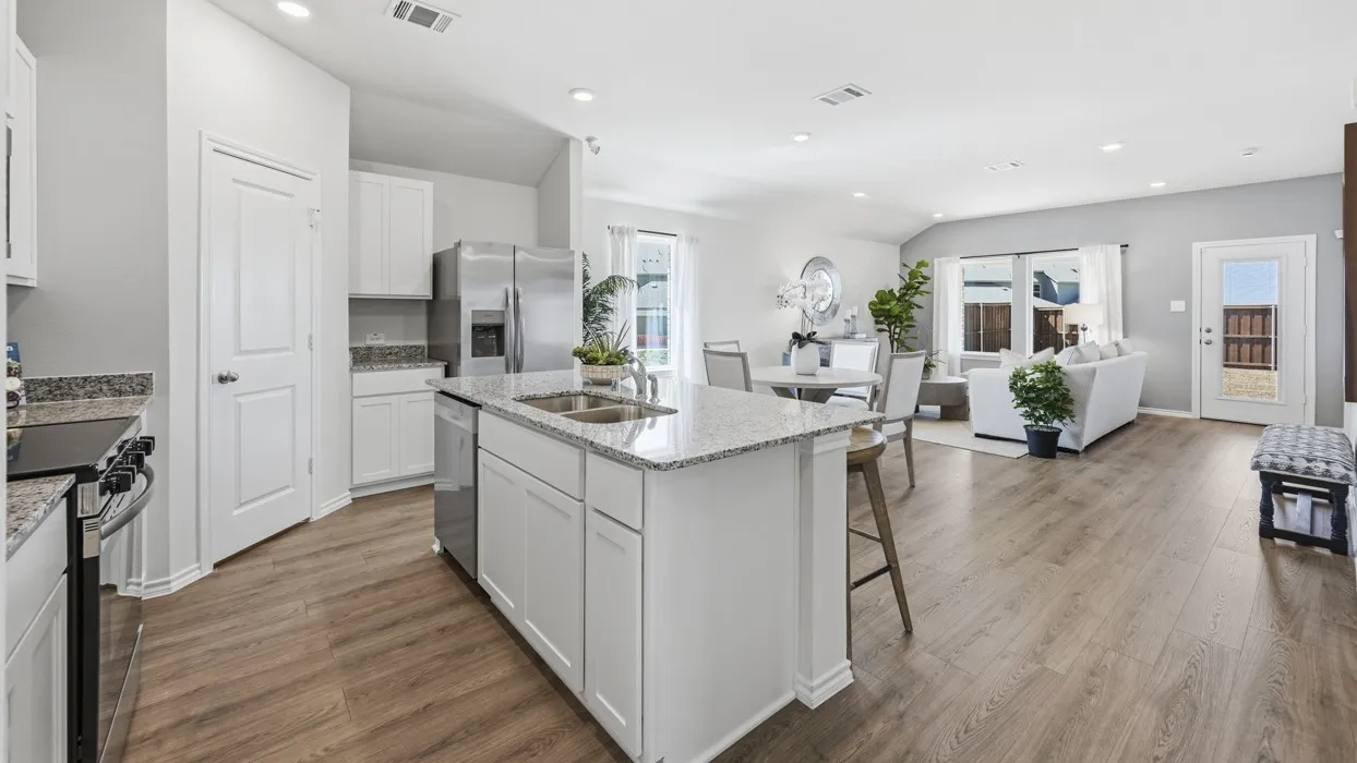 Open-concept living area featuring wood-finish flooring throughout, a central kitchen island with a double sink, stainless steel appliances, and abundant natural light from multiple windows