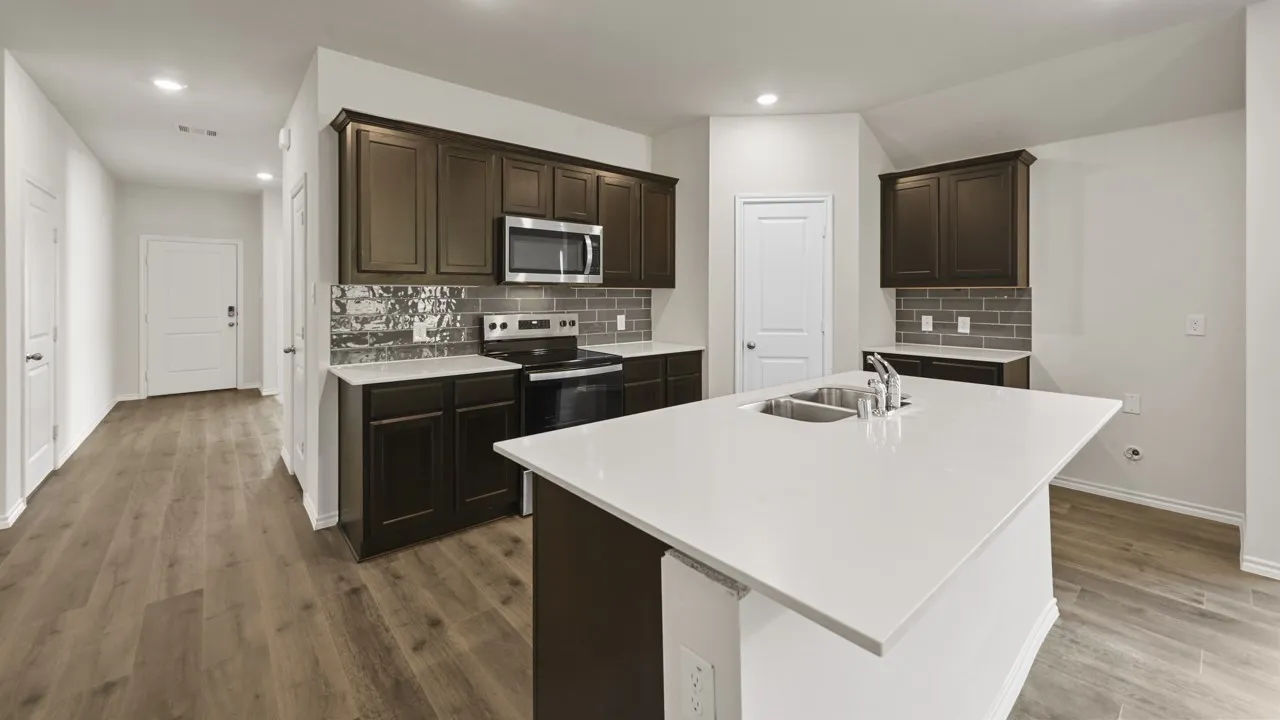 Kitchen featuring a large island with an undermount double-basin sink, light-toned countertops, dark wood cabinetry, stainless steel appliances, and a gray subway tile​​‌​​​​‌​​‌‌​‌‌​​​‌‌​‌​‌​‌​​​‌​​ backsplash