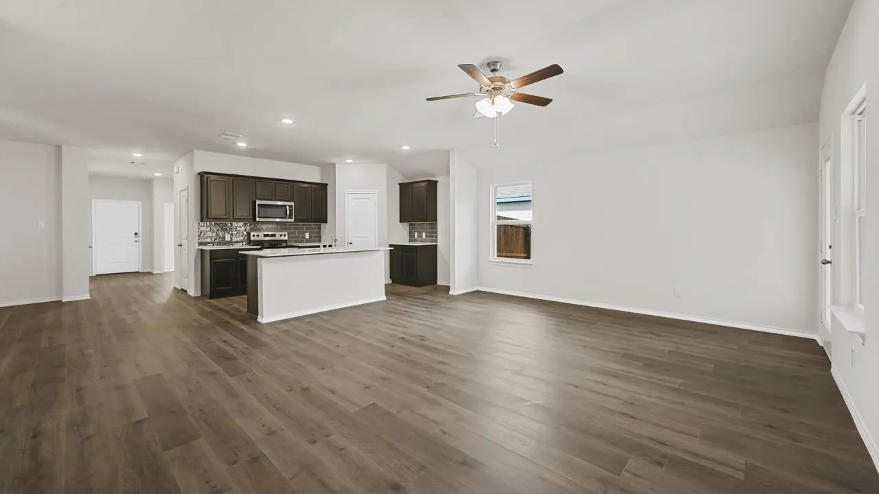 Open-concept living space featuring wood-finish flooring, a kitchen island with seating, dark wood cabinetry, and stainless steel appliances