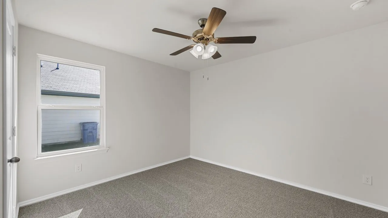 Neutral wall paint complemented by plush carpeting, a single window, and a ceiling fan with integrated lighting