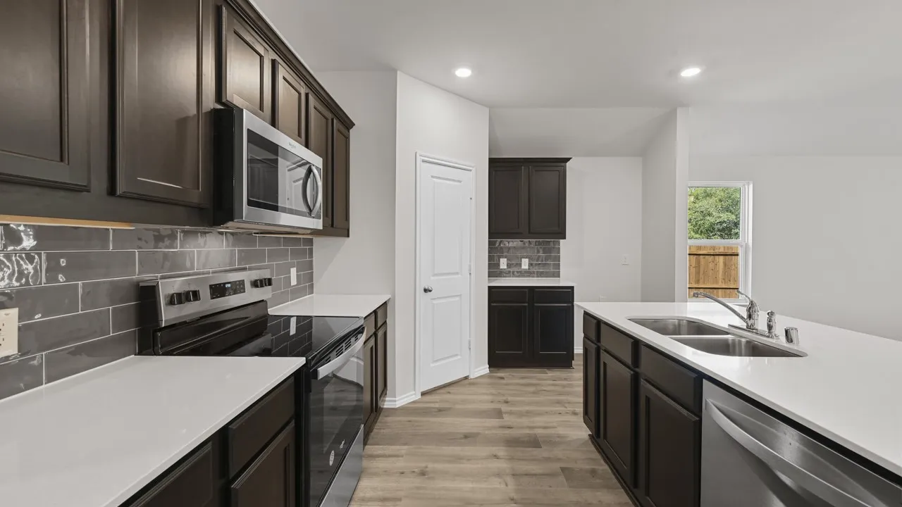 Modern kitchen featuring dark wood-finish cabinetry, stainless steel appliances, a center island with a double sink, light countertops, and wood-finish flooring