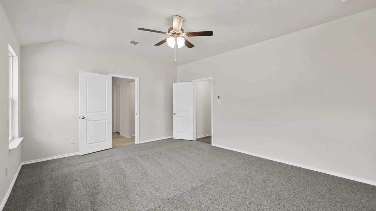Spacious room featuring vaulted ceilings, a ceiling fan with integrated lighting, plush grey carpeting, and white interior doors