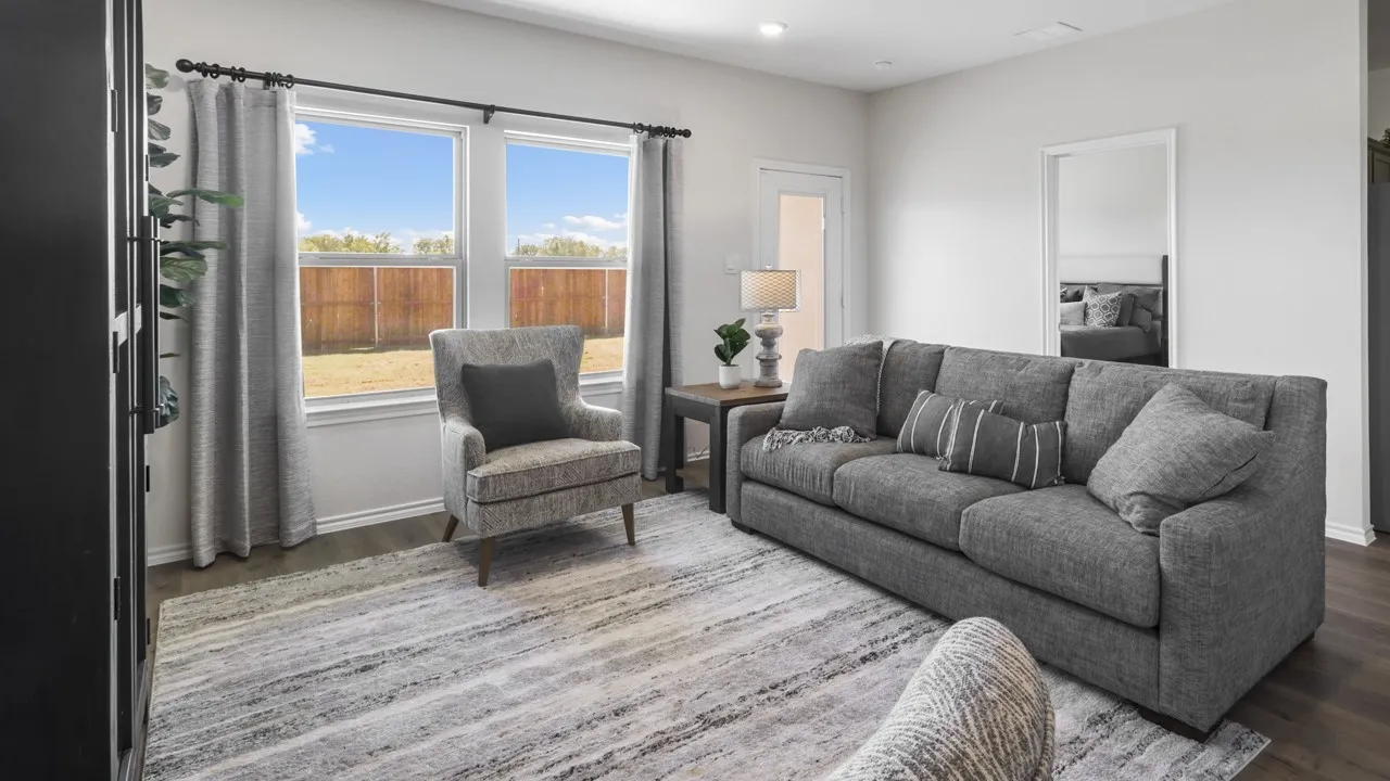 Bright living area featuring wood-finish flooring, white walls, and a pair of large windows overlooking a fenced backyard