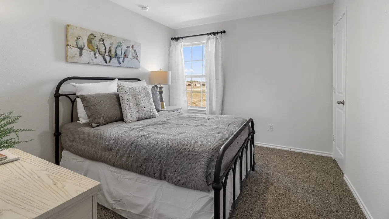 Bedroom featuring light-toned walls, carpeted flooring, and a single window with white curtains