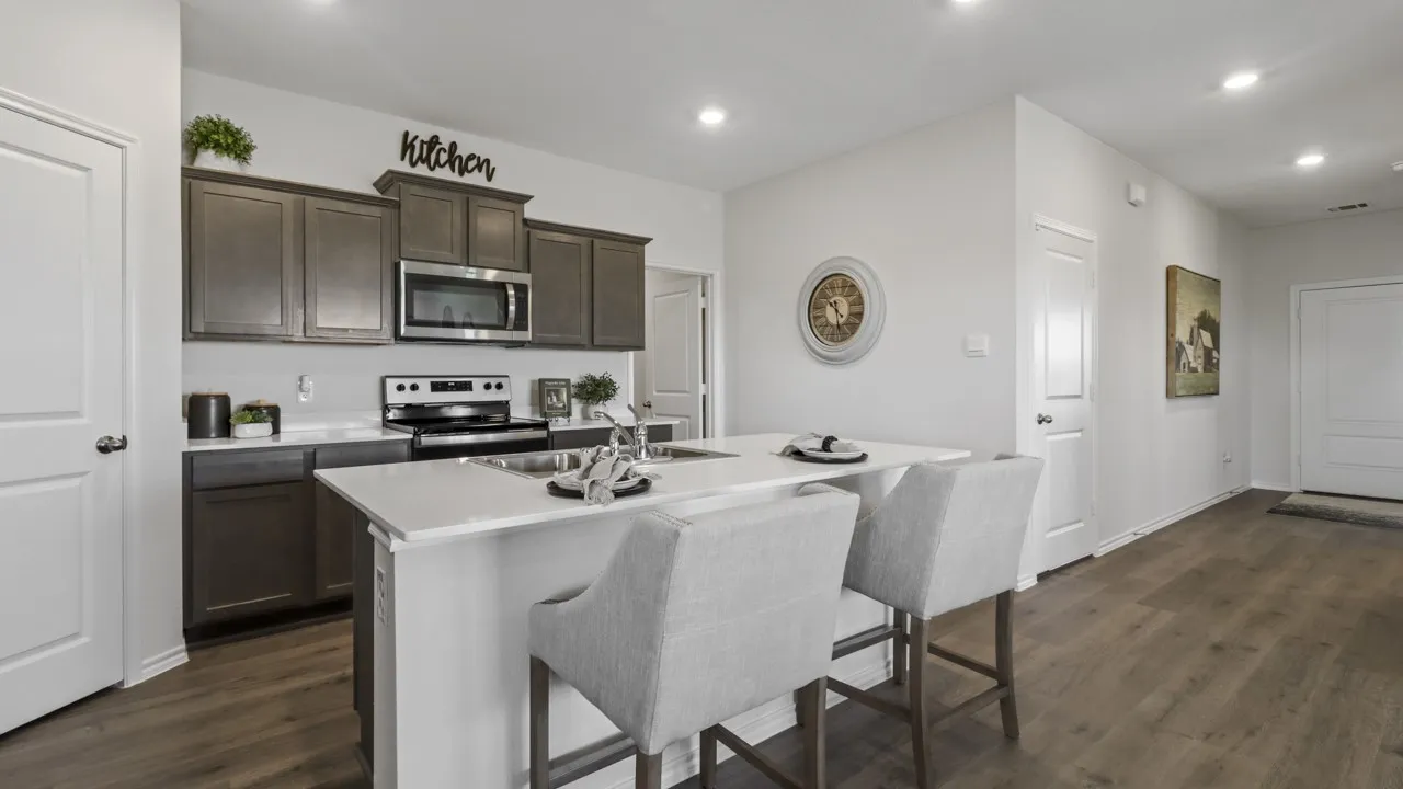 Kitchen featuring dark wood-finish cabinetry, stainless steel appliances, a white countertop island with a double basin sink, and wood-finish flooring