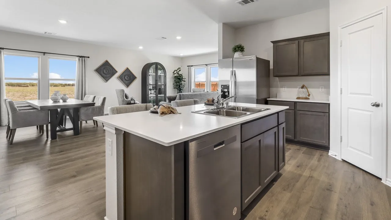 Kitchen island with integrated double basin sink and stainless steel dishwasher, contrasting dark cabinetry, white countertops, and wood-finish flooring