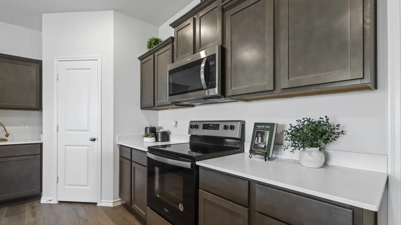 Kitchen featuring dark wood-finish cabinetry, light-toned countertops, and stainless steel appliances including a microwave and range
