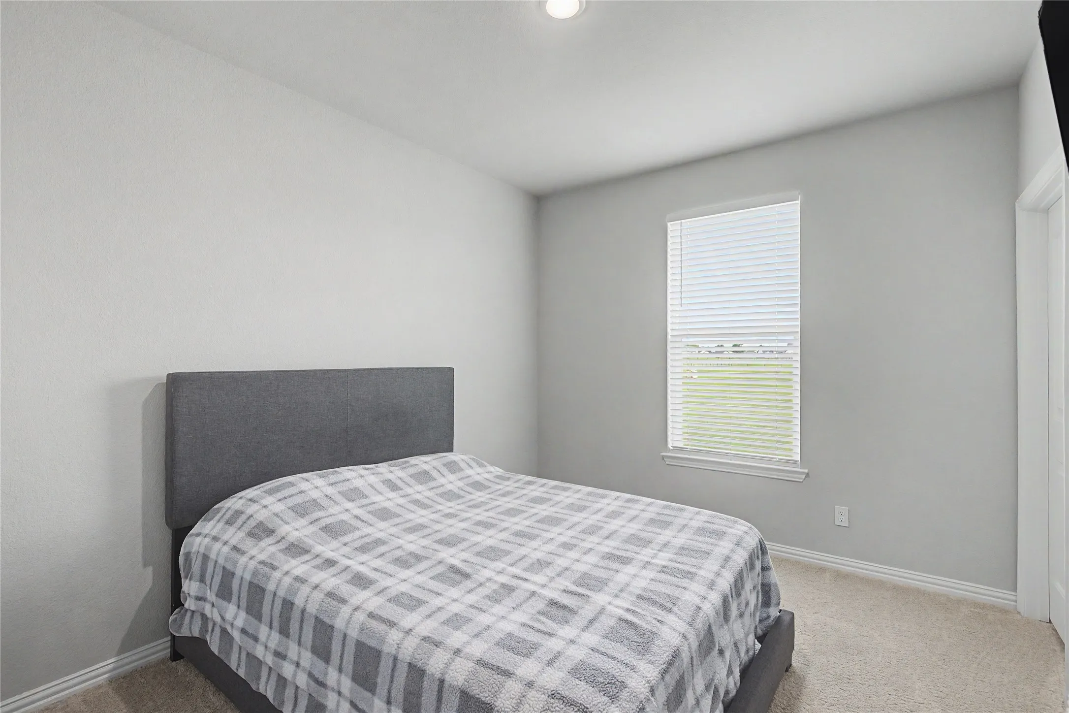 Carpeted room featuring a single window with blinds, light gray walls, and white baseboards