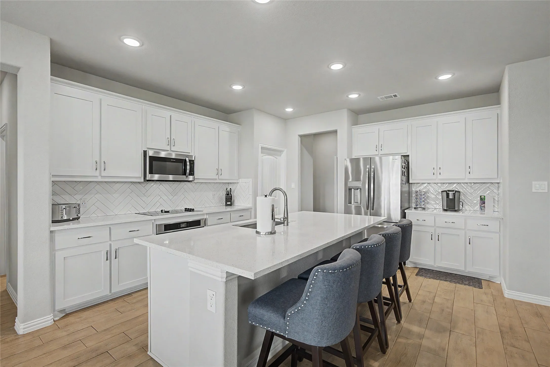 Kitchen featuring light wood-finish flooring, white cabinetry, integrated stainless steel appliances, a herringbone tile backsplash, and a large central island with a solid surface countertop