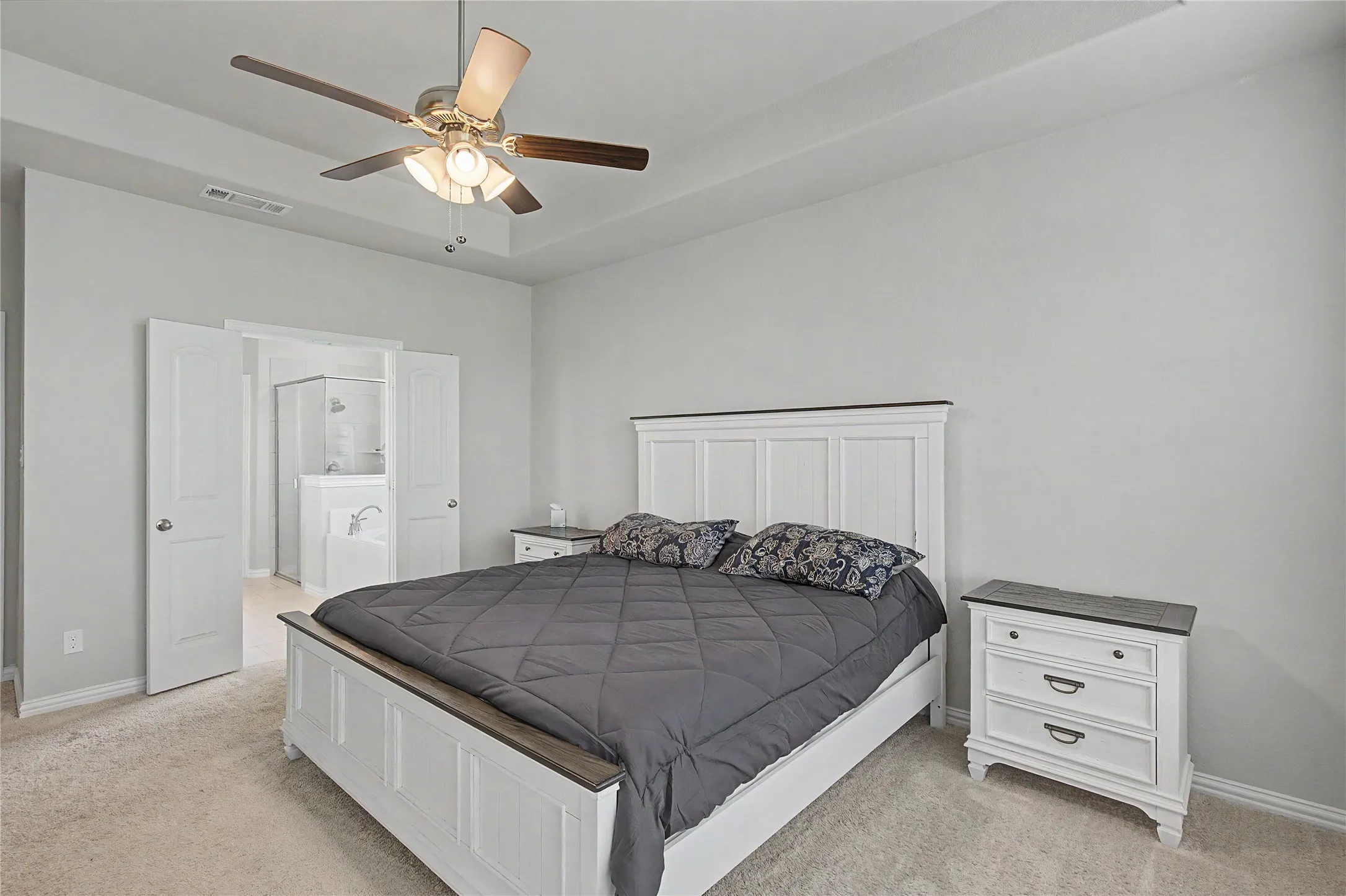 Carpeted bedroom featuring a tray ceiling with a ceiling fan, light gray wall paint, and white trim