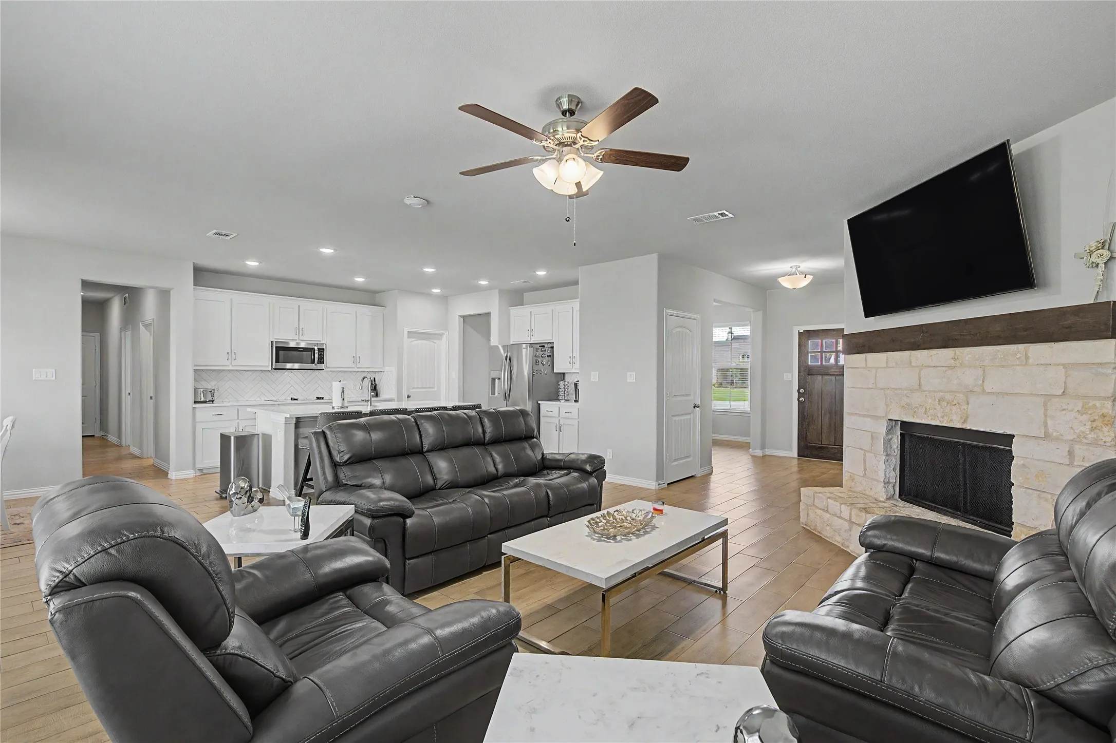 Open-concept living space featuring wood-finish flooring, a stone fireplace with a wood mantle, and a ceiling fan