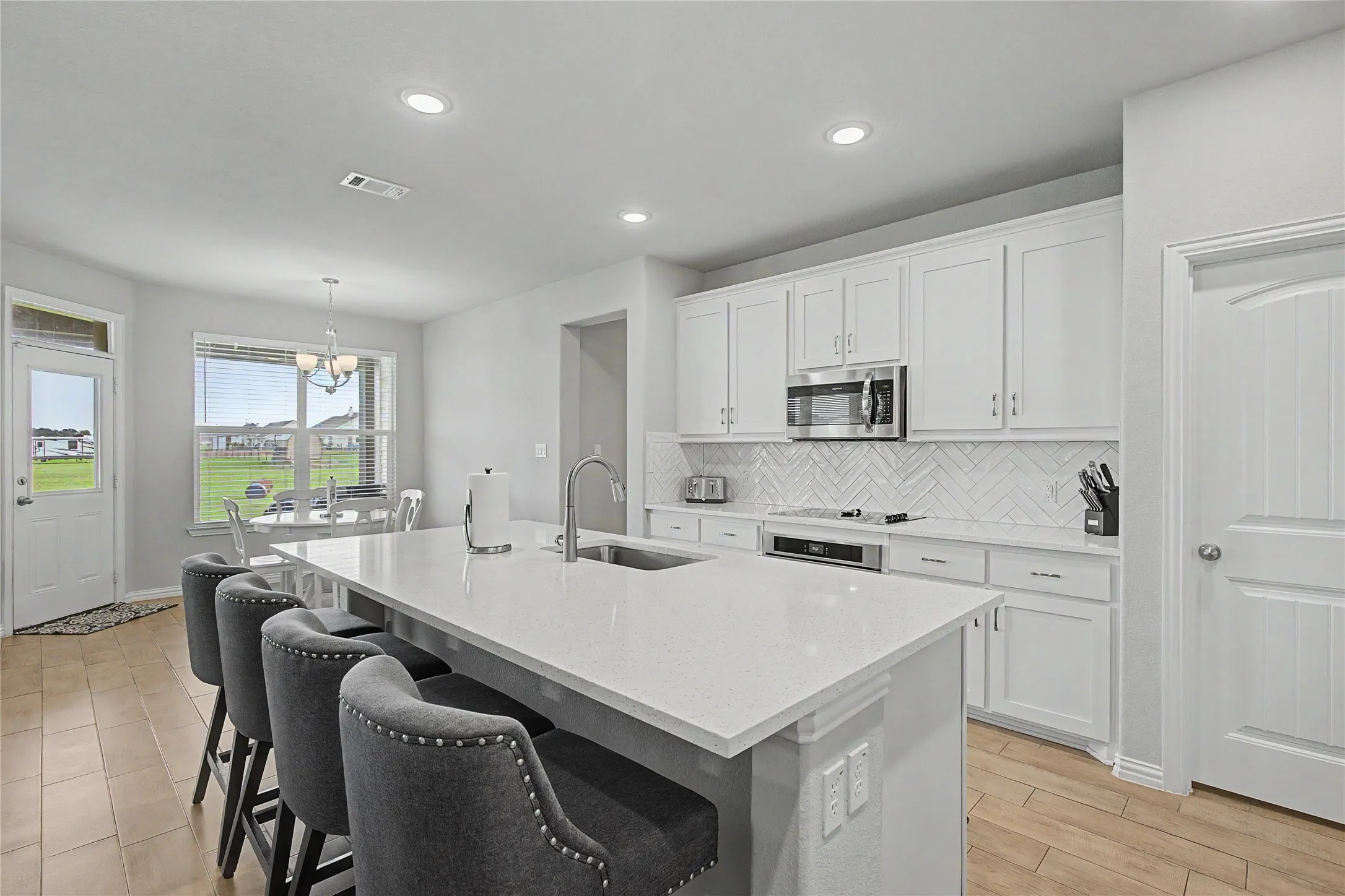 Spacious kitchen featuring a large island with sink, quartz countertops, white shaker cabinetry, stainless steel appliances, and a herringbone tile backsplash