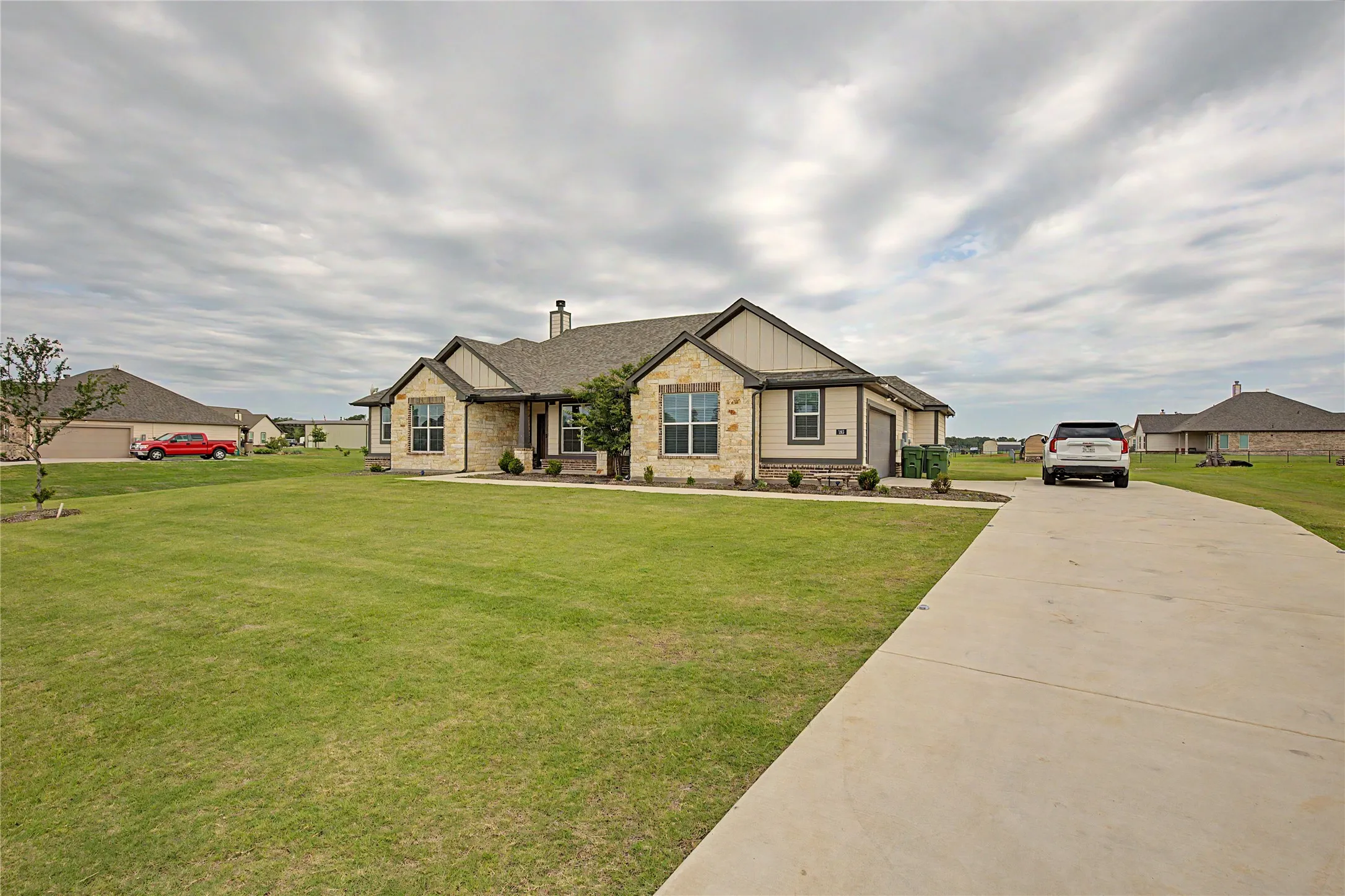 Stone and siding exterior with a concrete driveway, established lawn, and landscaping
