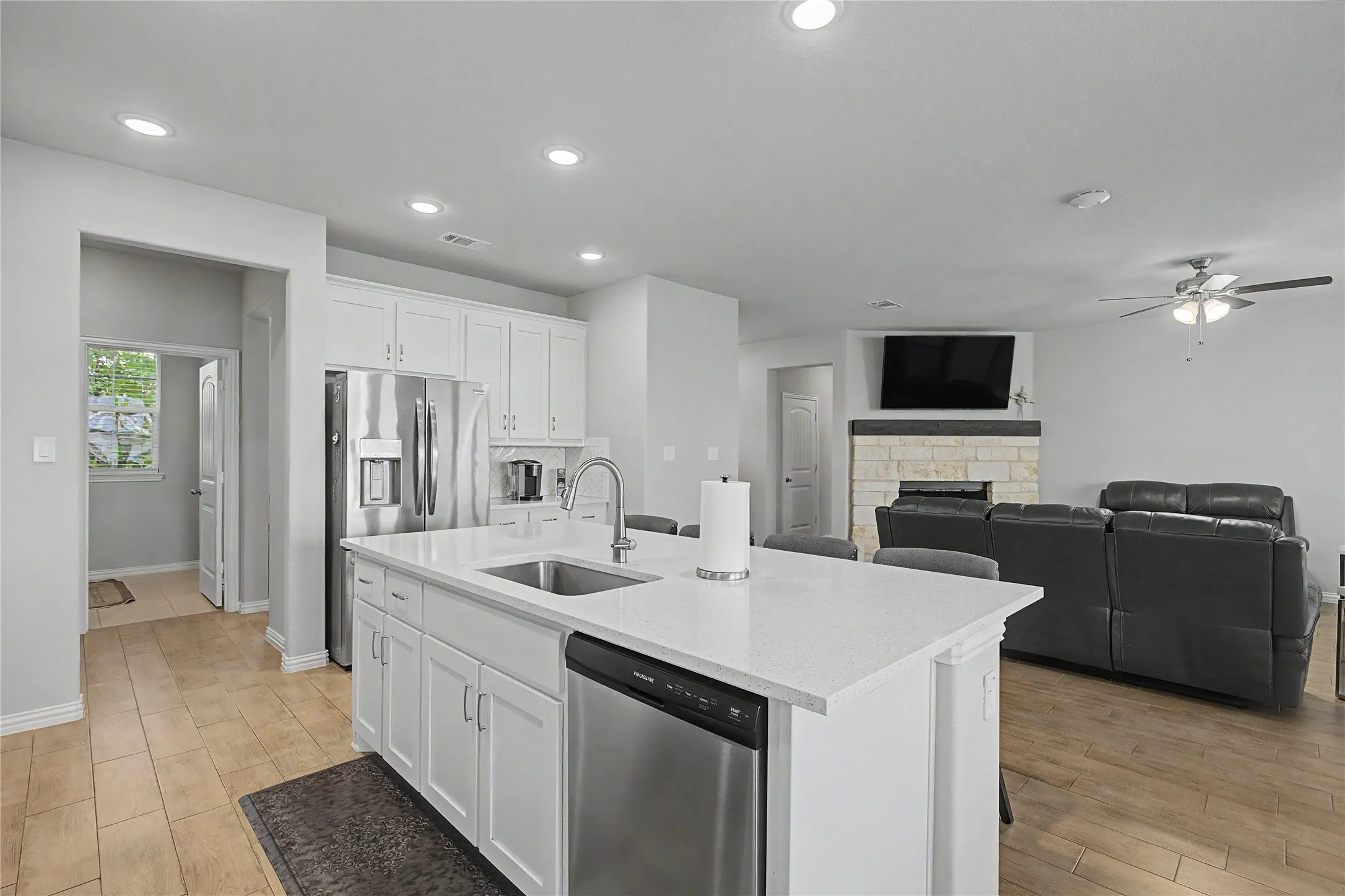 Open-concept kitchen featuring white cabinetry, stainless steel appliances, a center island with sink, and light-toned countertops