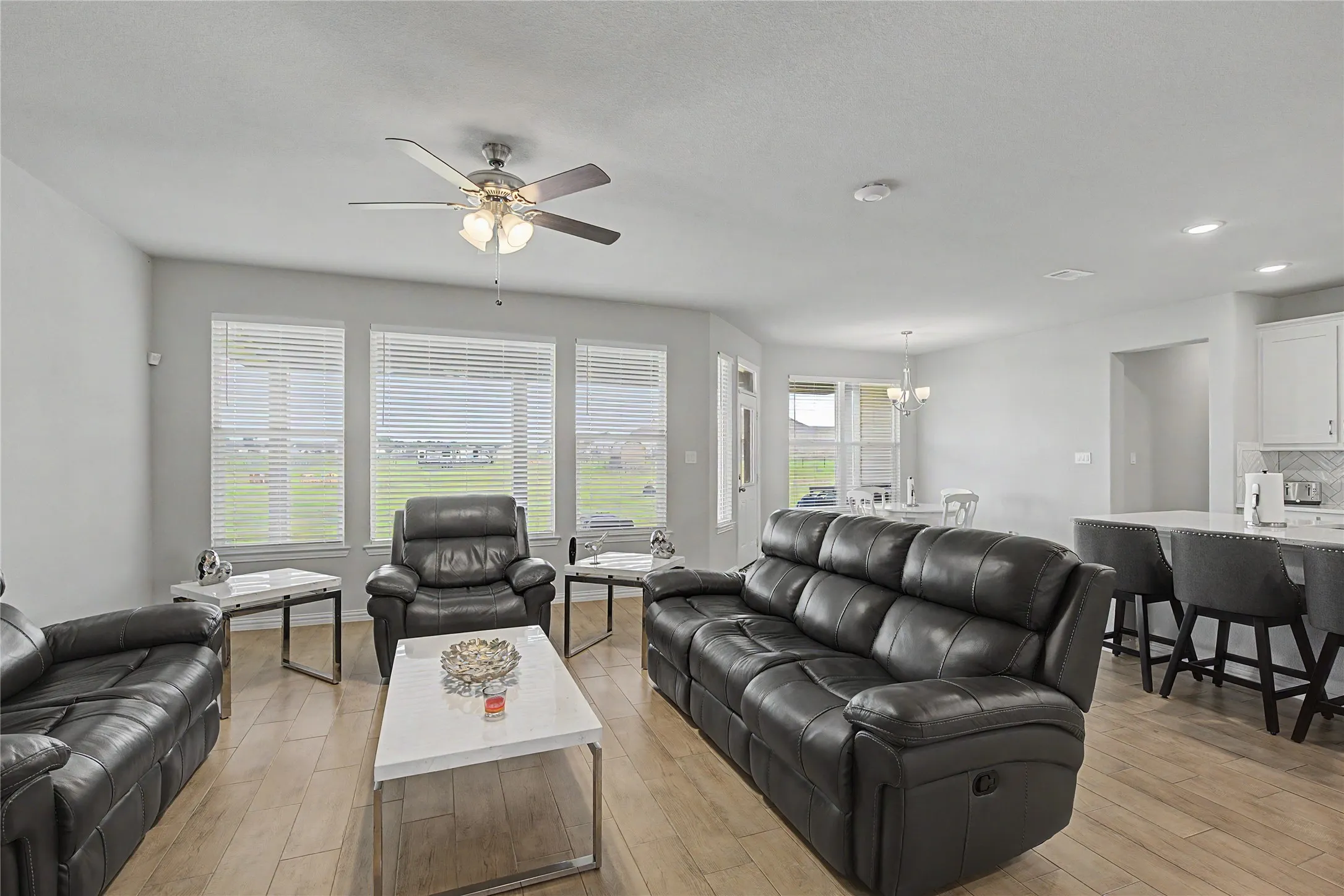 Open-concept living area featuring a ceiling fan with integrated lighting, wood-finish flooring, and white window blinds