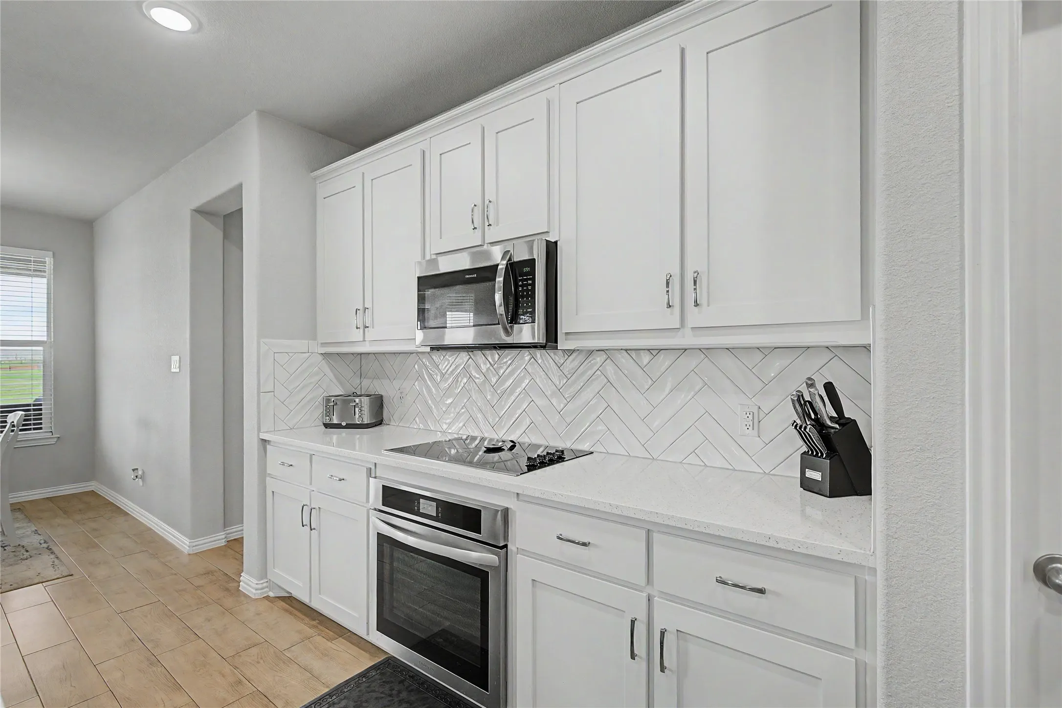 Bright kitchen featuring white shaker cabinetry, stainless steel microwave, and an integrated oven