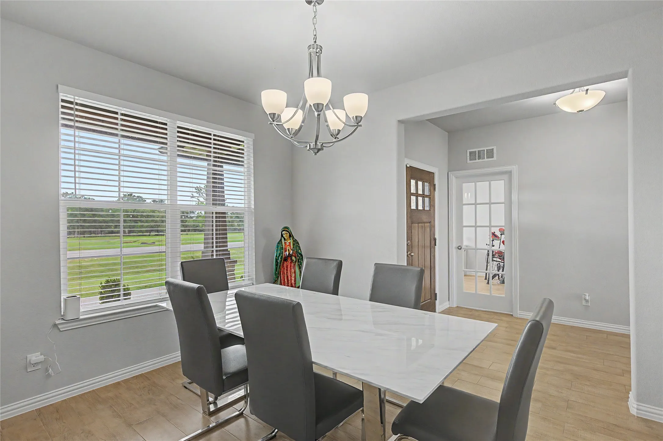 Dining area featuring wood-finish flooring, a large window with horizontal blinds, and a contemporary chandelier