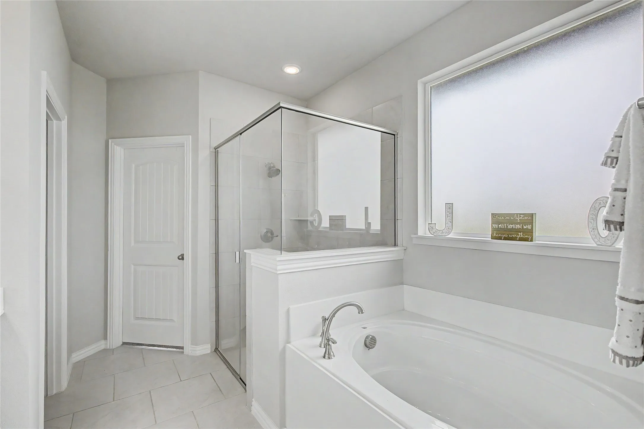 Bathroom featuring a standalone soaking tub with brushed nickel fixtures, a glass-enclosed shower, a frosted privacy window, and tile flooring