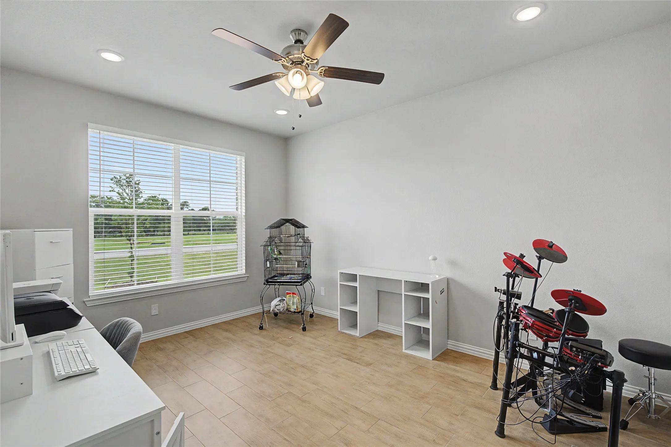 Spacious room featuring wood-finish flooring, a large window with horizontal blinds, and a ceiling fan with integrated lighting