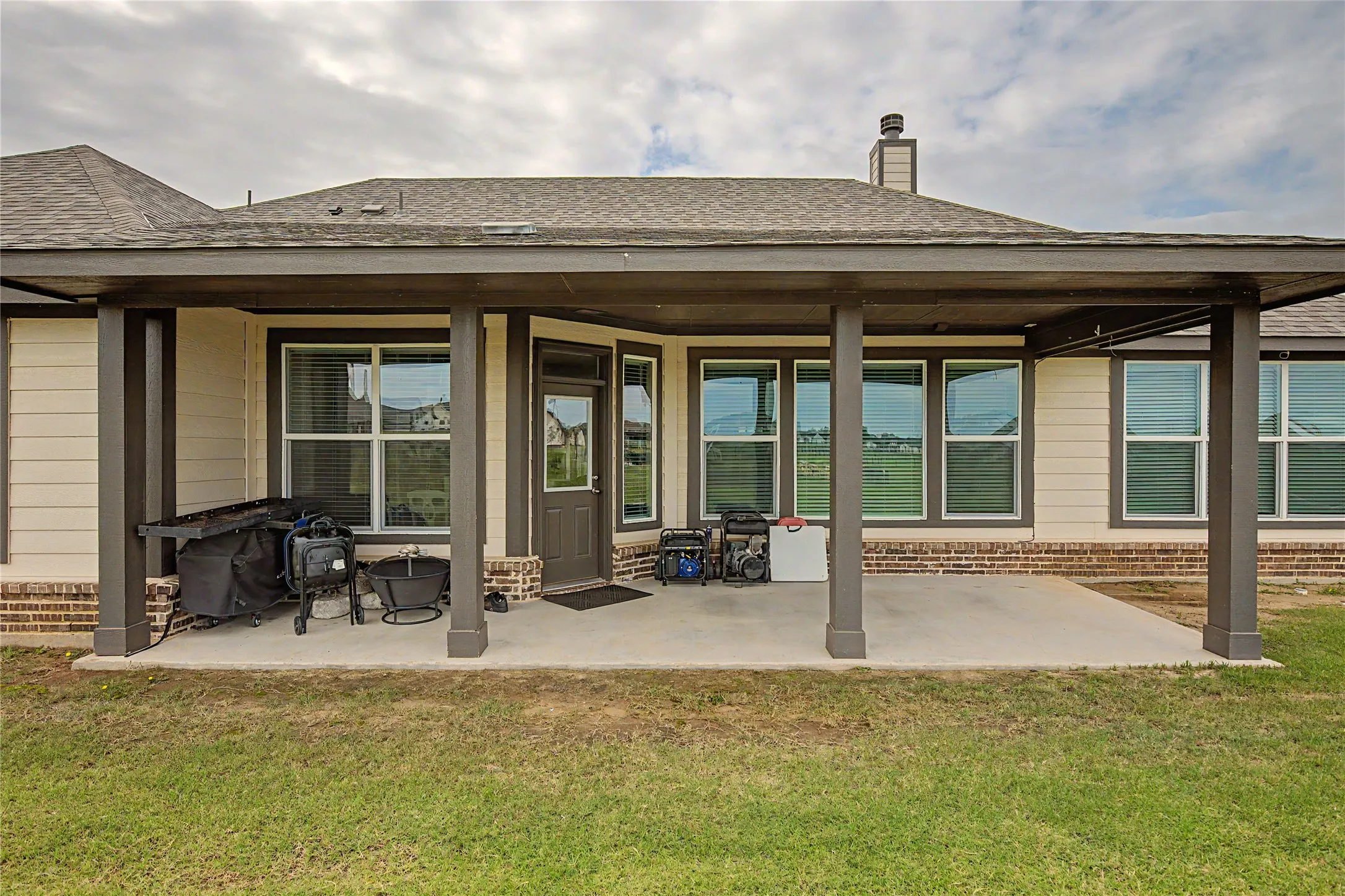 Covered concrete patio with dark wood-finish support columns and a gray shingle roof