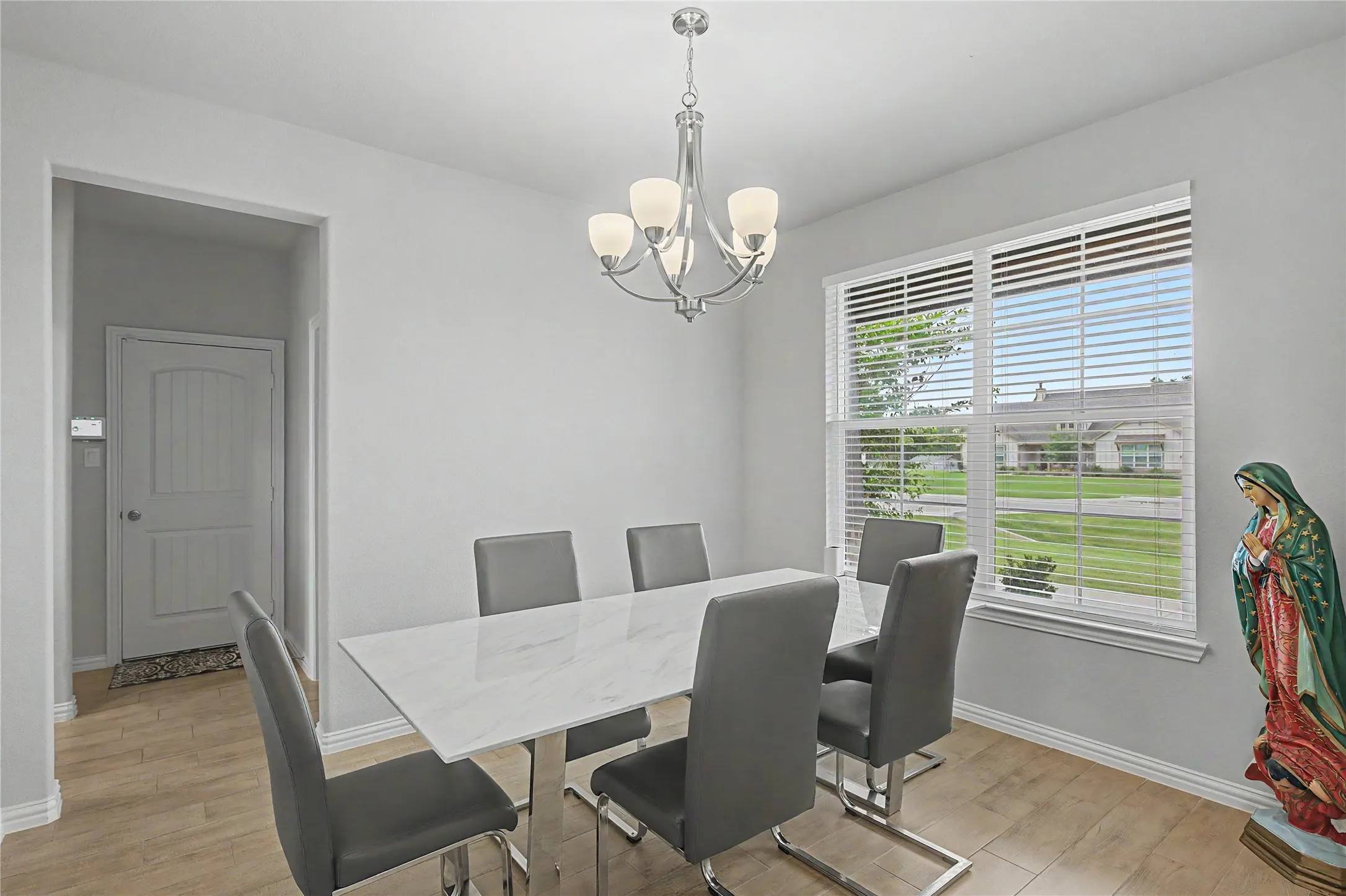 Dining area featuring wood-finish flooring, a contemporary chandelier, and a large window with blinds
