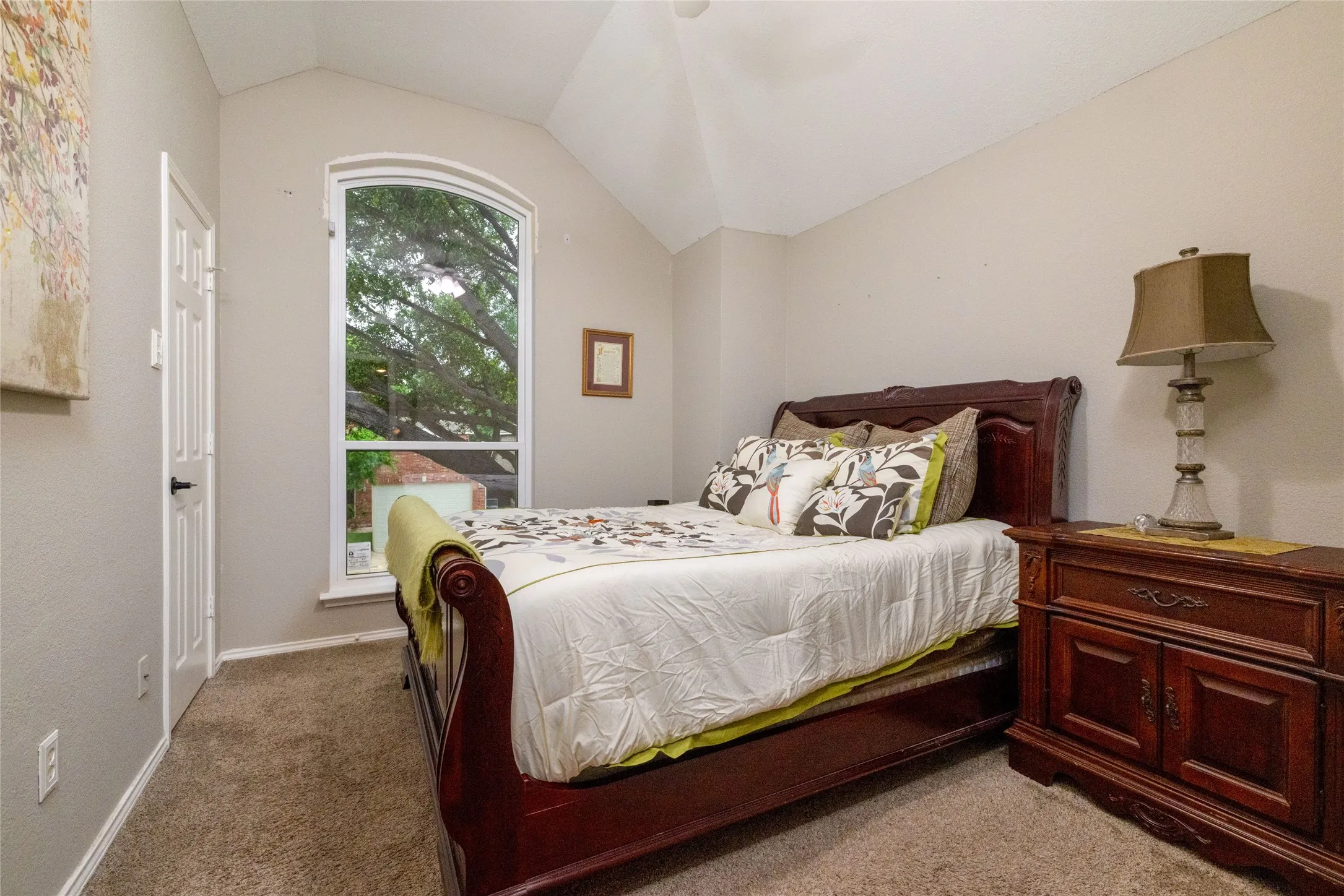 Vaulted ceilings enhance this room, featuring an arched window, light neutral wall tones, and plush carpet flooring
