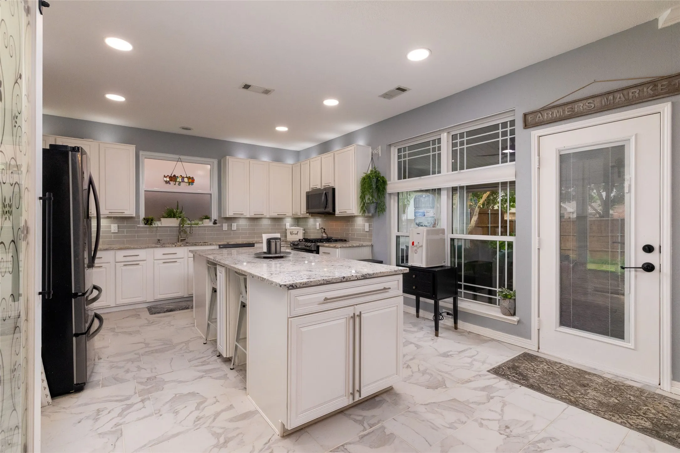 Spacious kitchen featuring an expansive center island with seating, white shaker-style cabinetry, granite countertops, a subway tile backsplash, and large windows
