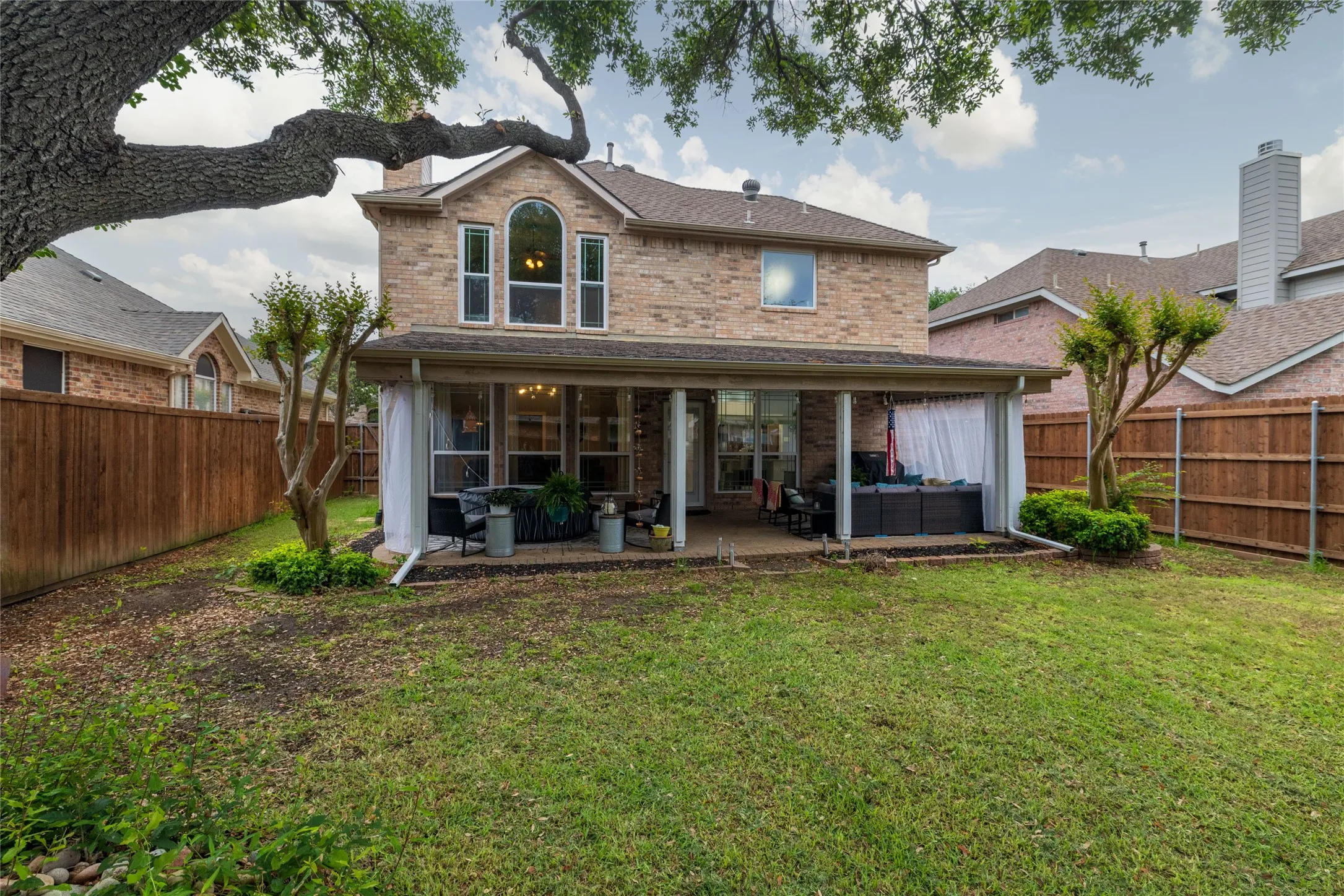 Brick exterior featuring an arched window, a covered patio, and a fenced backyard with mature trees