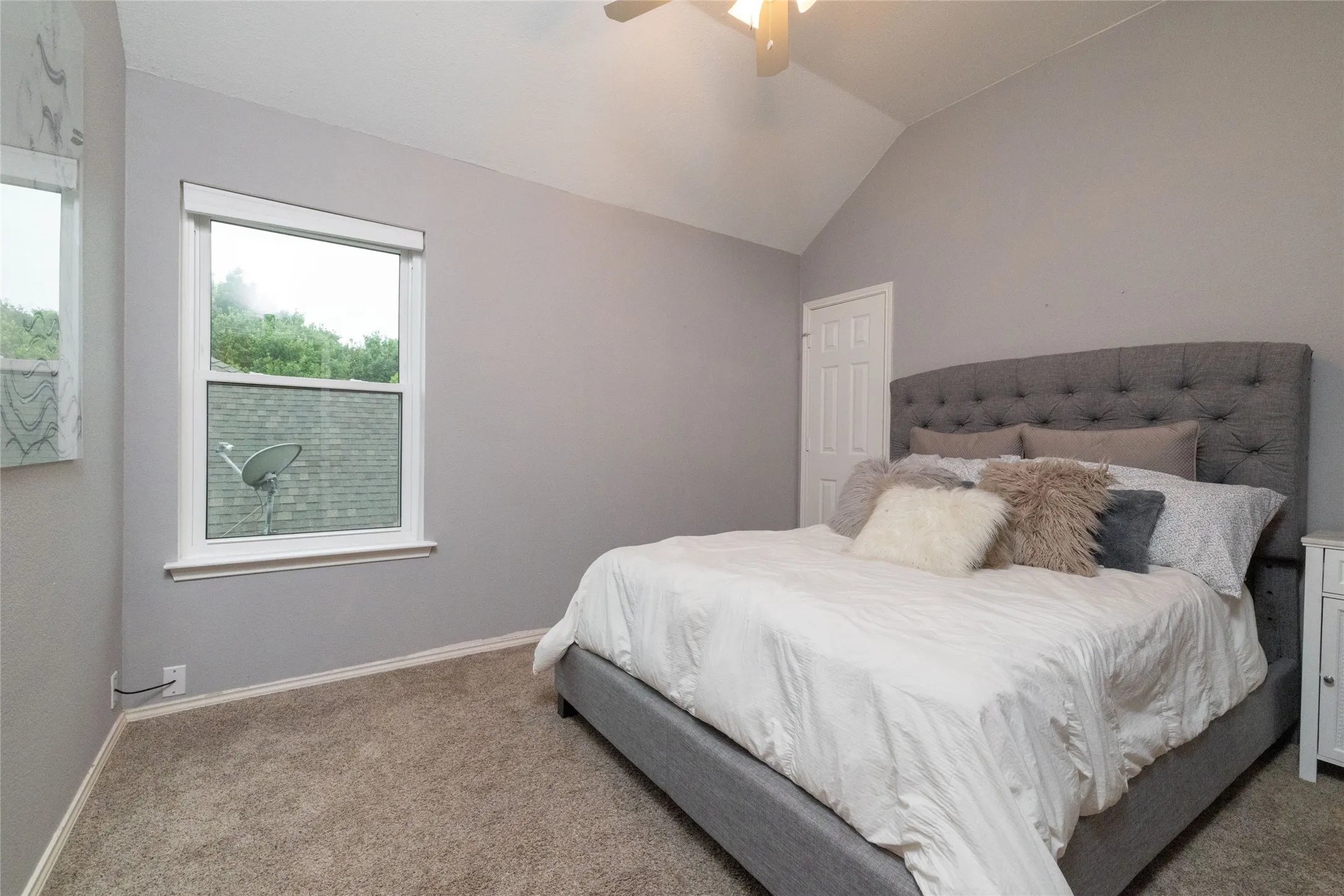 Carpeted bedroom featuring an angled vaulted ceiling, single window with white trim, and a white paneled door