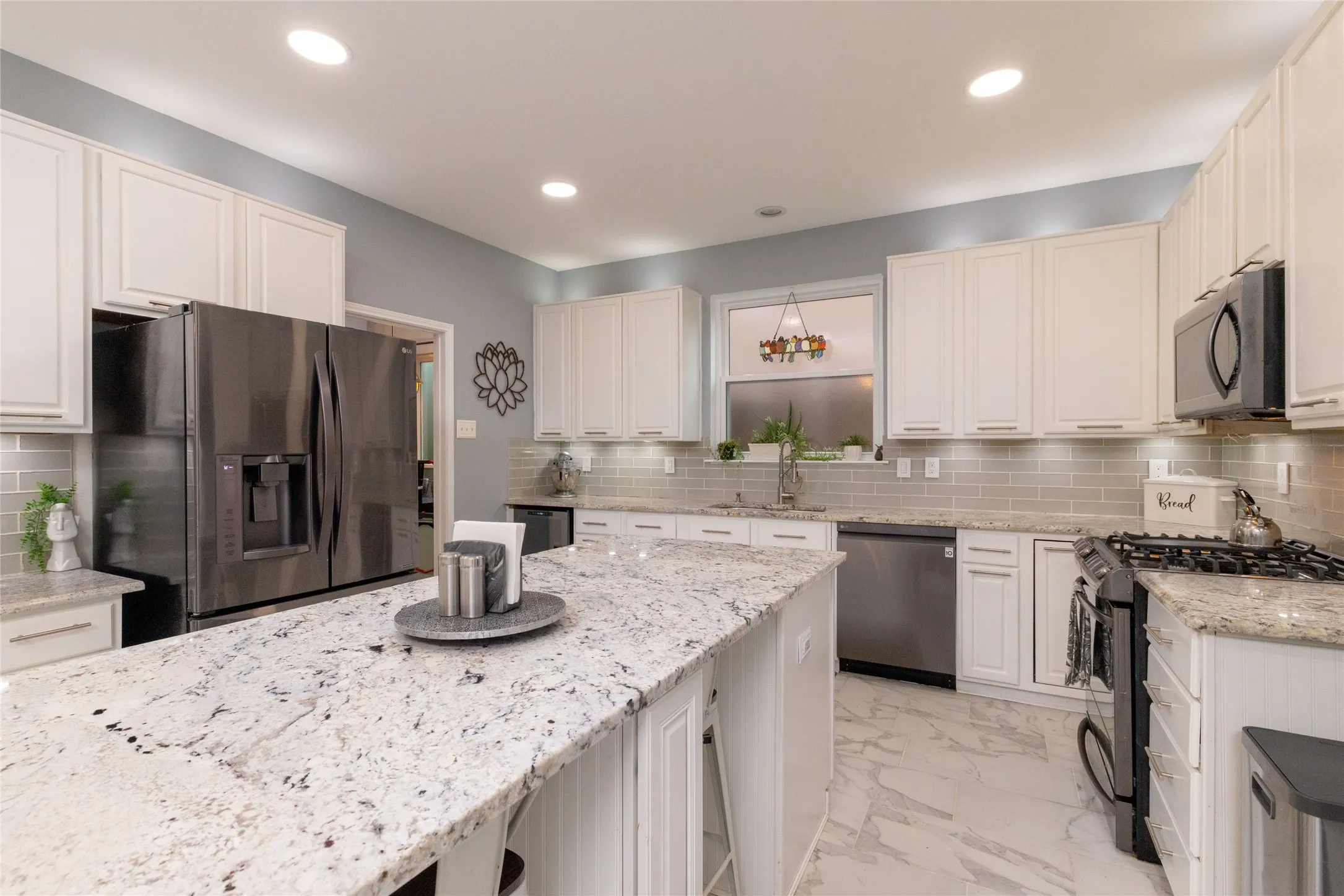 Gourmet kitchen featuring a large central island with a granite countertop, white shaker cabinetry, stainless steel appliances, and a subway tile backsplash
