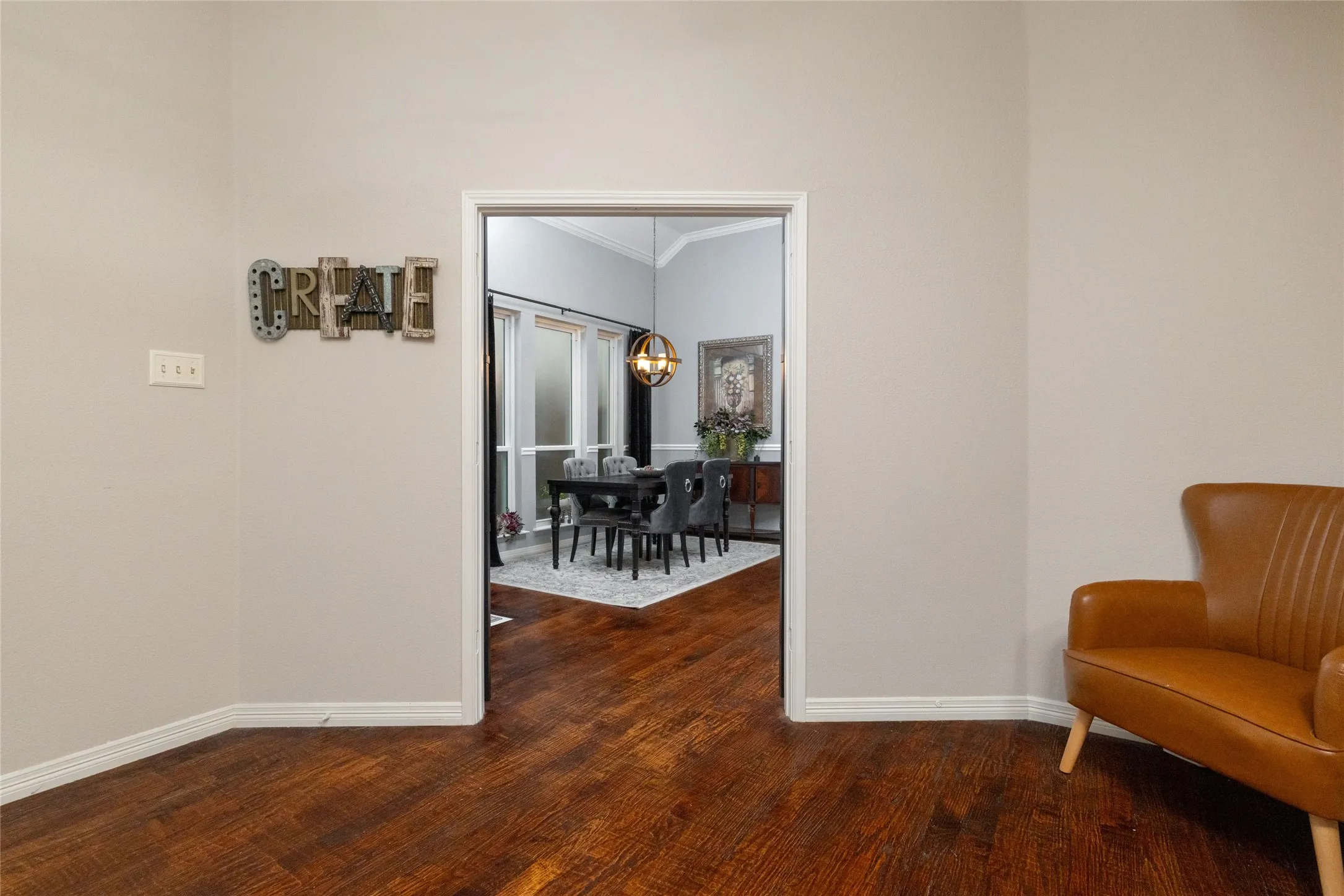 Hardwood-style flooring extends through a wide doorway into a formal dining area featuring a vaulted ceiling with crown molding and an orbital chandelier