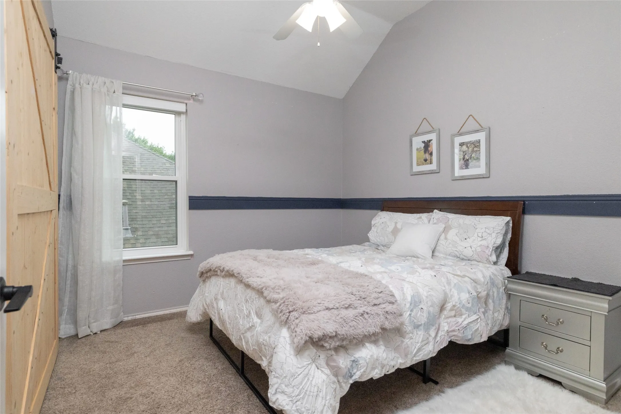Vaulted ceiling bedroom with a single window, carpet flooring, and a barn-style sliding door