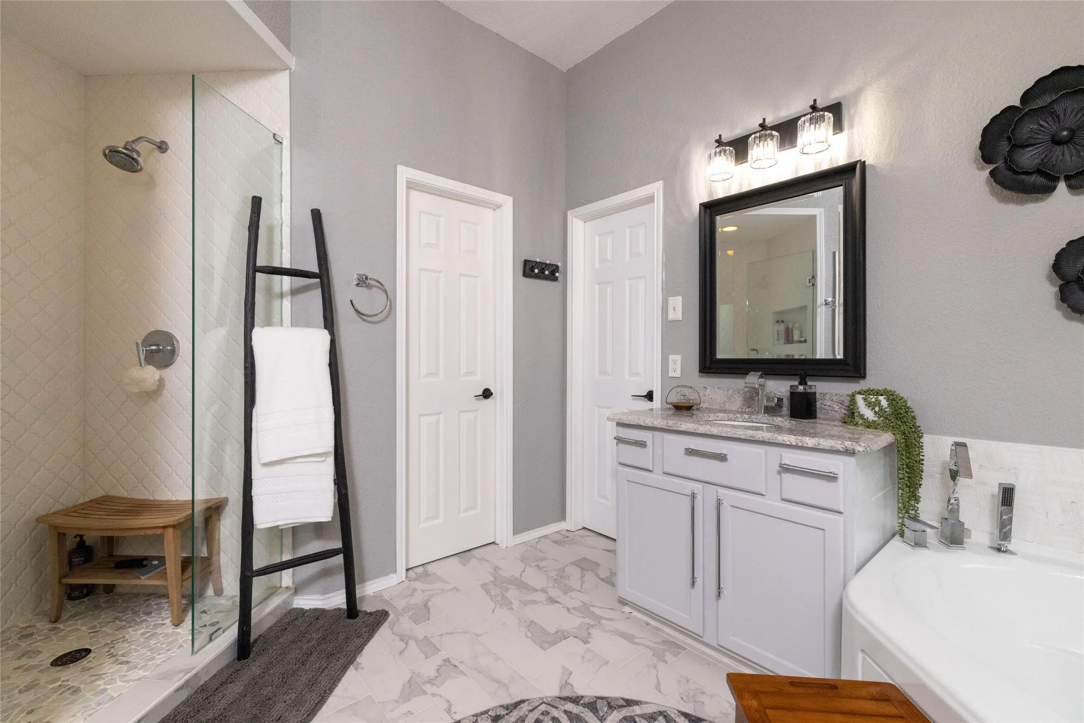 Bathroom featuring a frameless glass shower enclosure with white tile surround, a built-in shower bench, a corner soaking tub, a single vanity with a granite countertop, and tile flooring