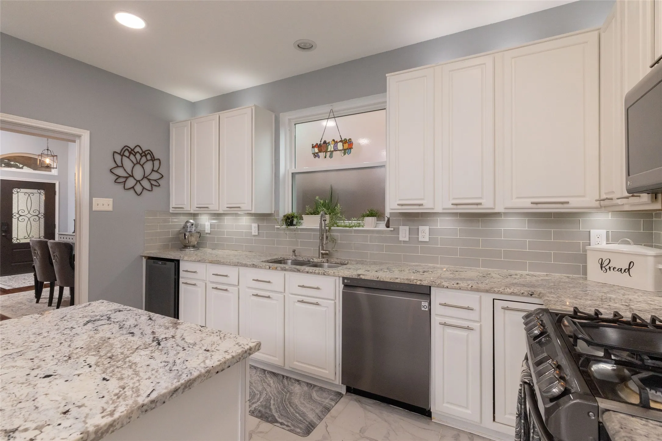 Kitchen featuring white cabinetry, light-toned granite countertops, a gray subway tile backsplash, stainless steel appliances, and recessed lighting
