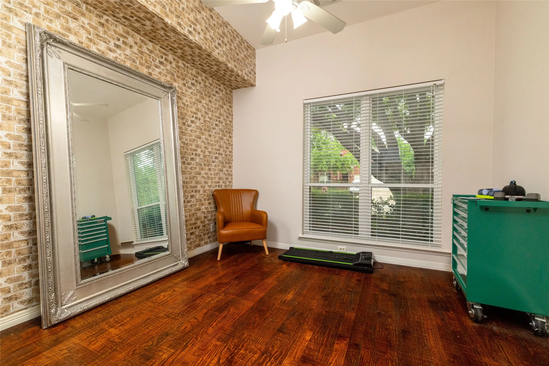 Interior space featuring wood-finish flooring, a large window with blinds, and a partial brick-patterned accent wall