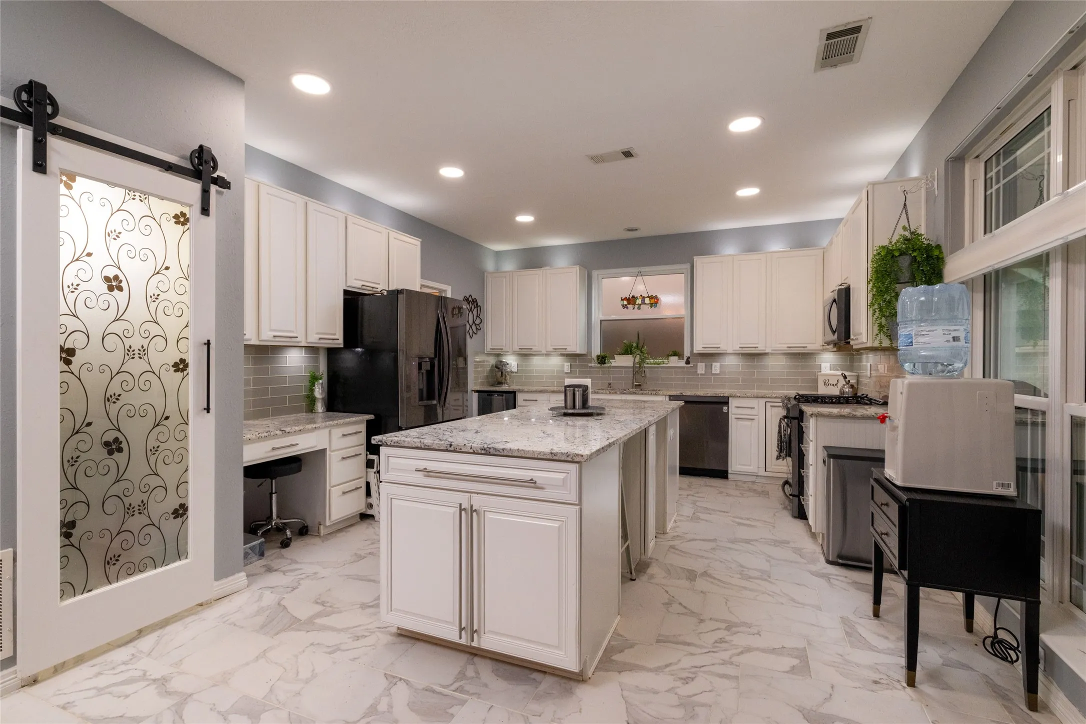 Spacious kitchen featuring an expansive center island with stone countertop, white cabinetry with silver hardware, light-colored tile flooring, and a barn door with etched glass