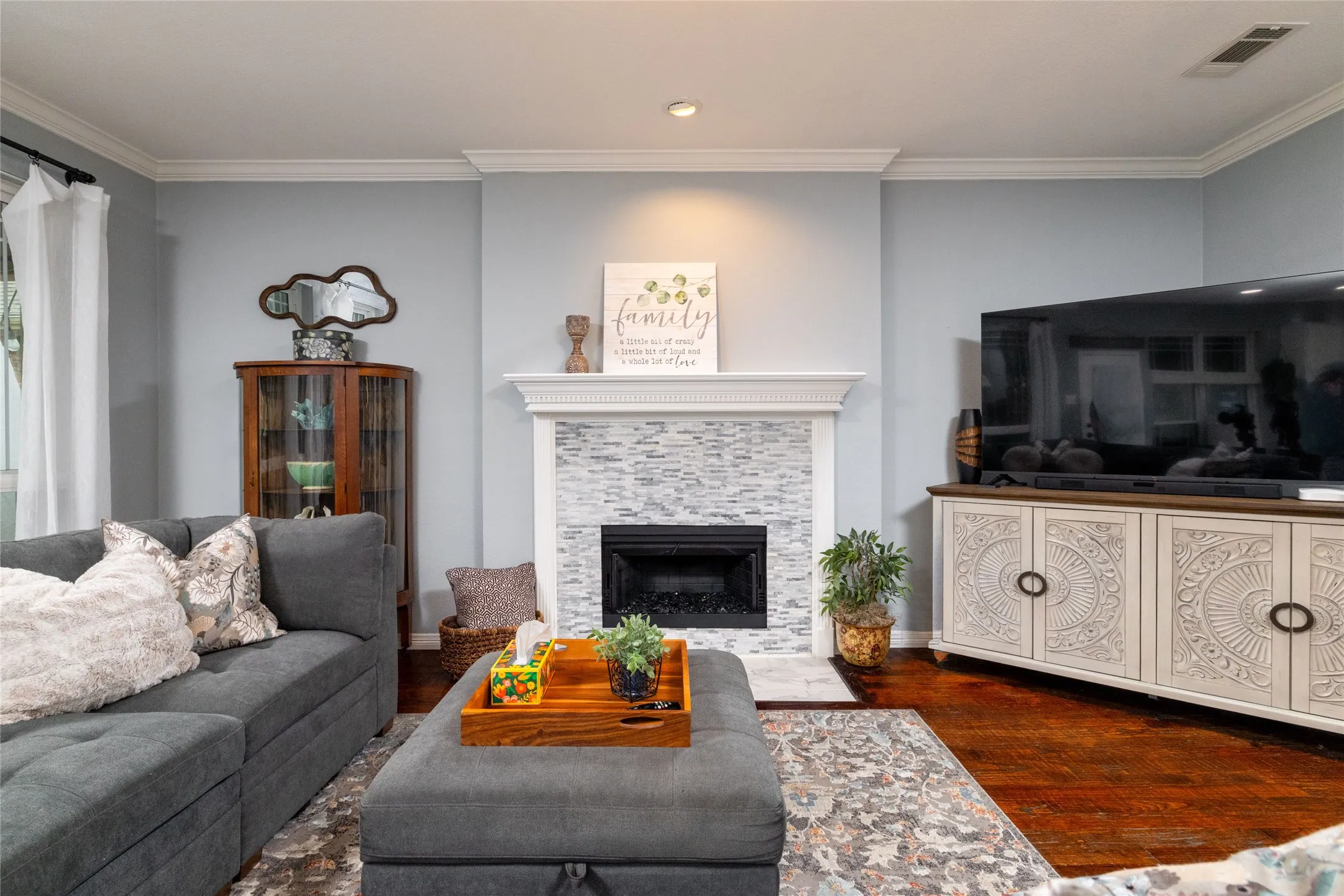 Living area featuring a fireplace with a stacked stone facade and white mantel, crown molding, recessed lighting, and wood-finish flooring