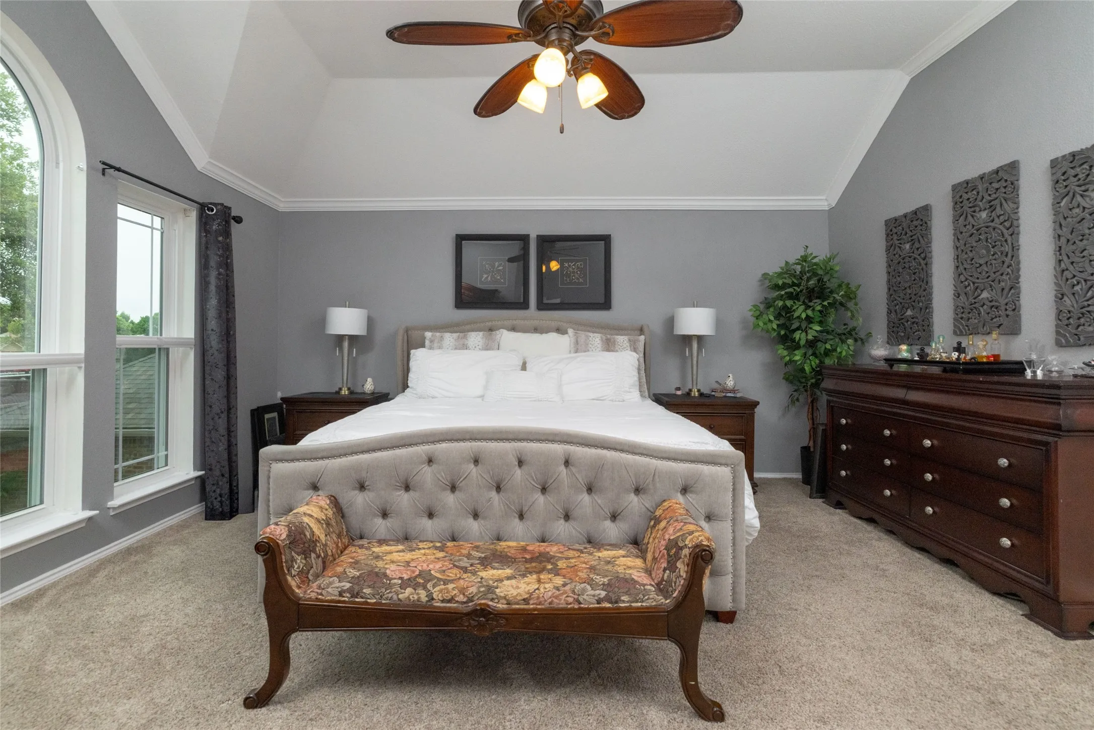 Vaulted ceiling with a ceiling fan, arched window, double hung window, wall-to-wall carpeting, and crown molding