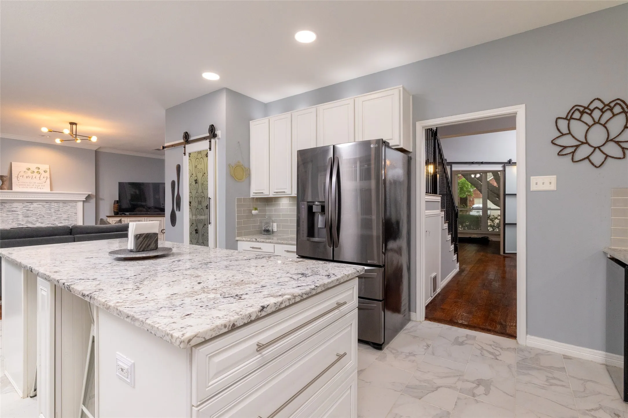 Kitchen featuring a light-toned island with a granite-style countertop, white cabinetry with silver hardware, a stainless steel refrigerator, and a light gray subway tile backsplash