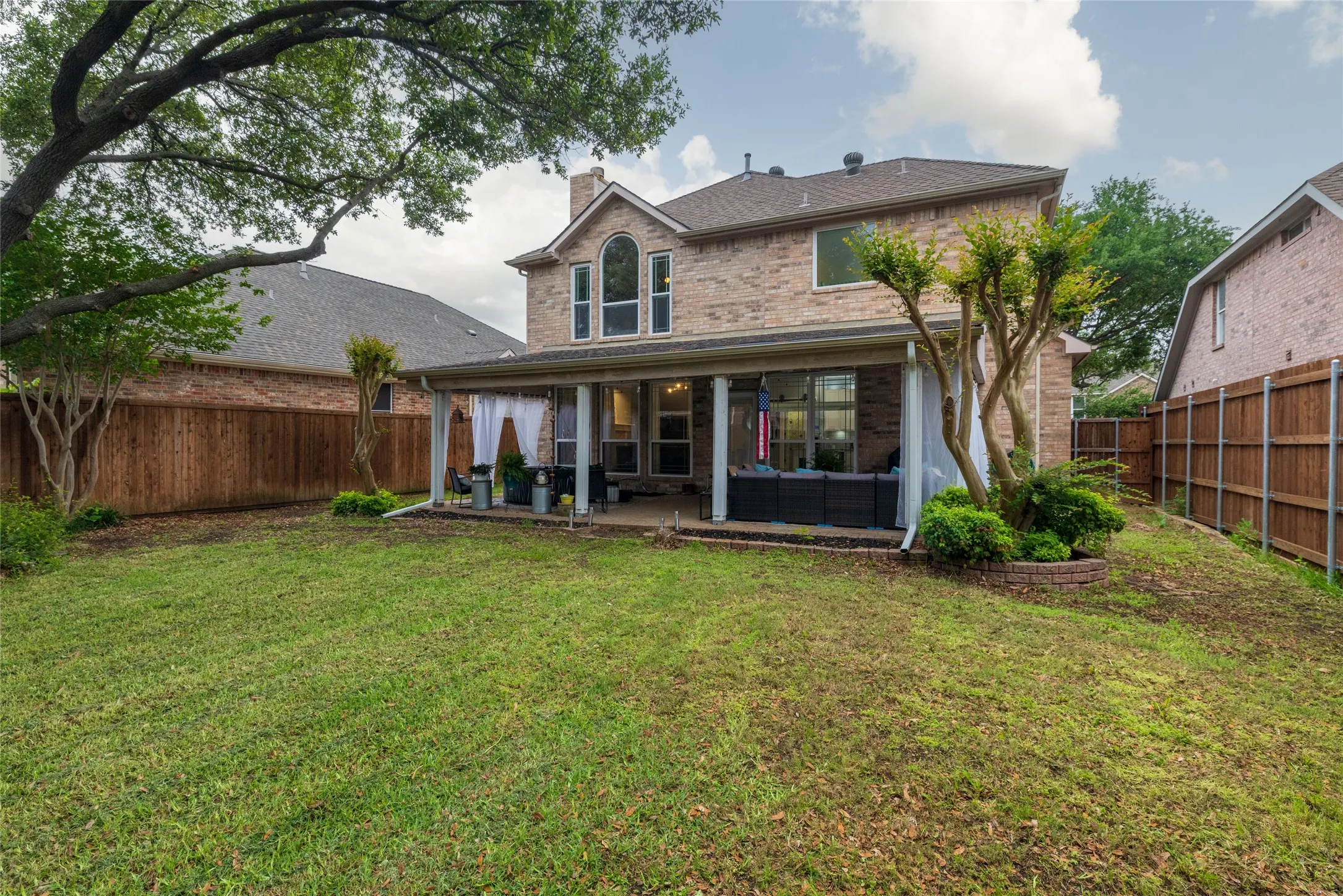 Expansive backyard featuring a covered patio with columns, a brick planter, and a privacy fence