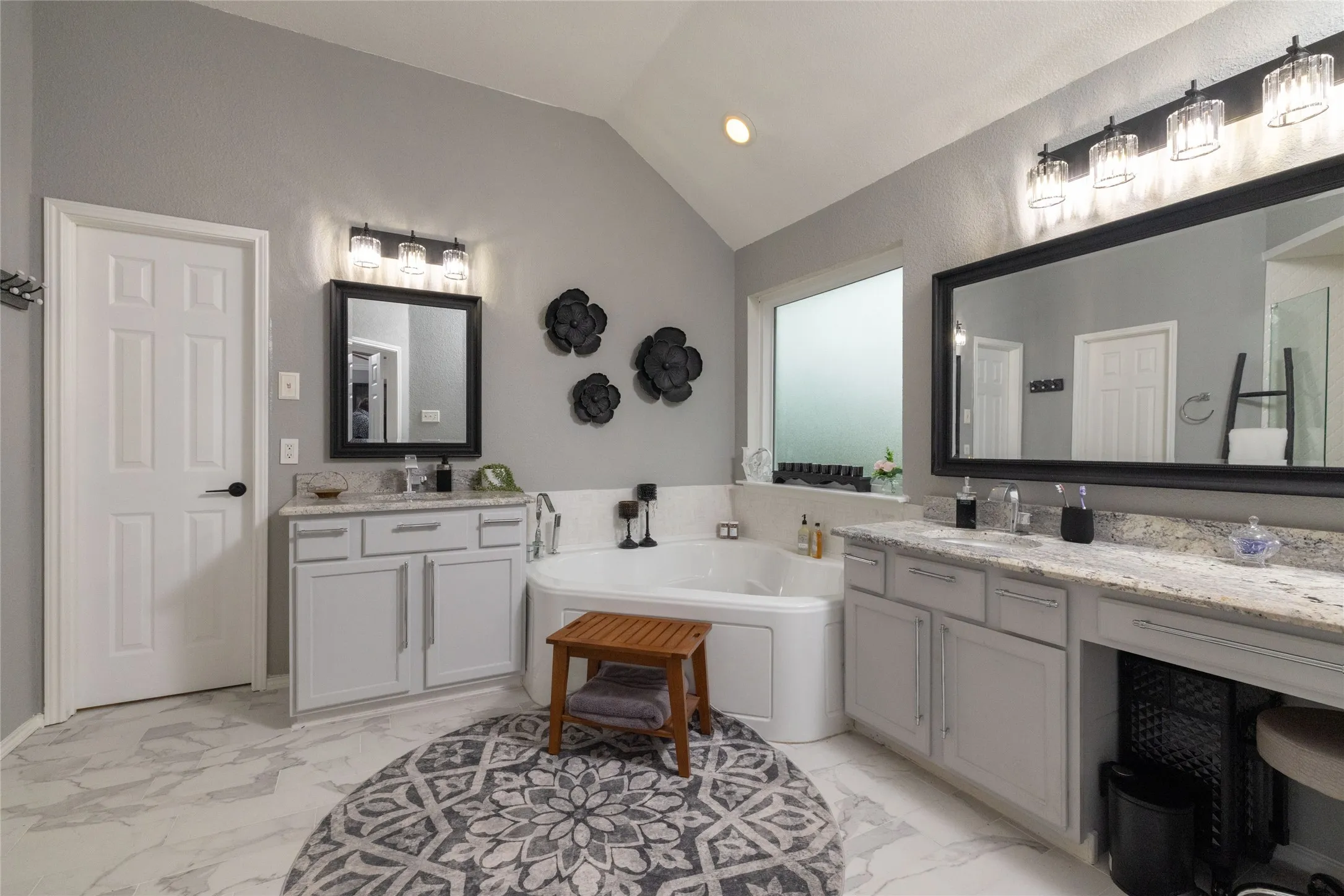 Spacious bathroom featuring a corner soaking tub, dual vanity with light-toned countertops, and marble-look flooring