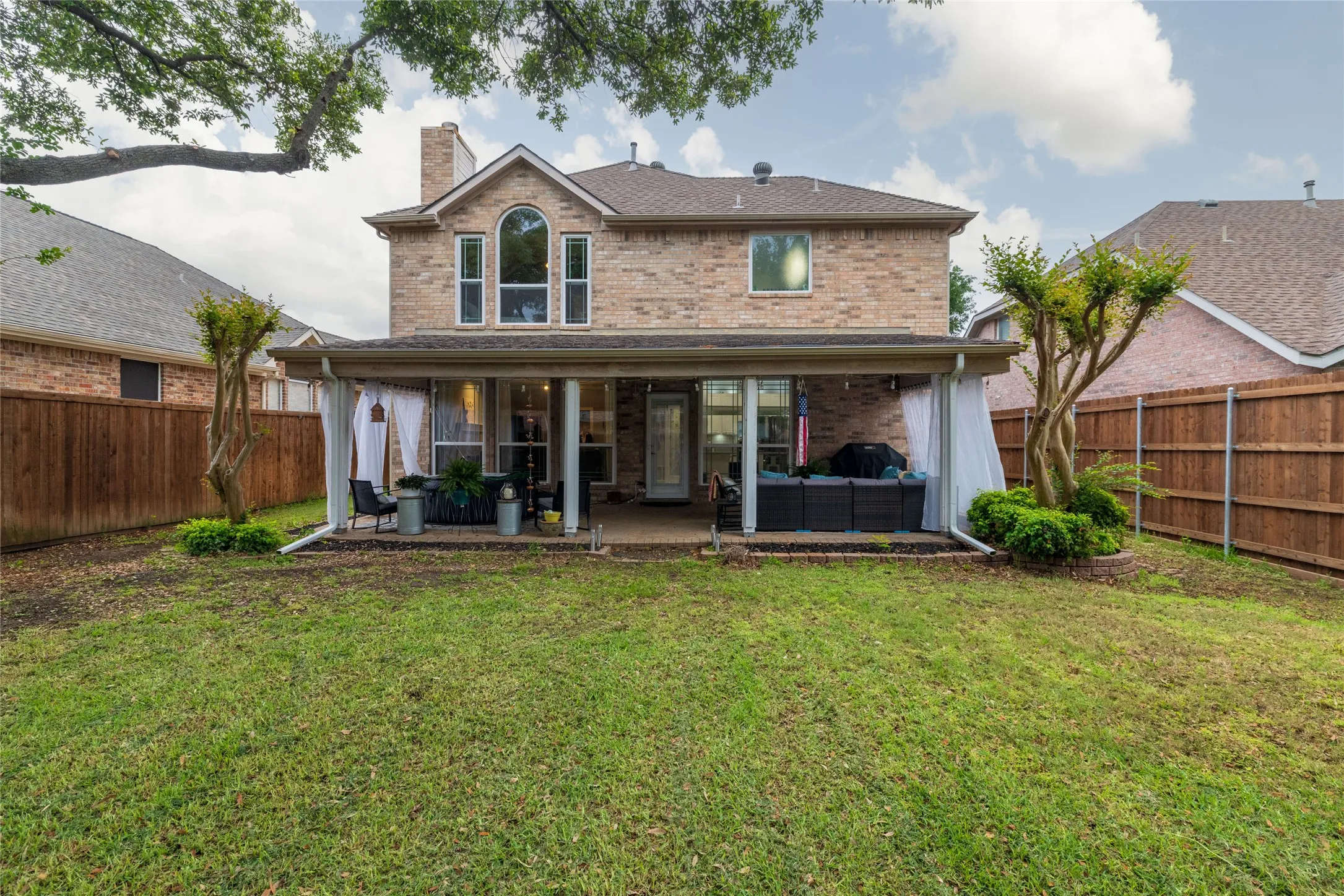 Brick exterior featuring a covered patio, extensive backyard, and mature trees